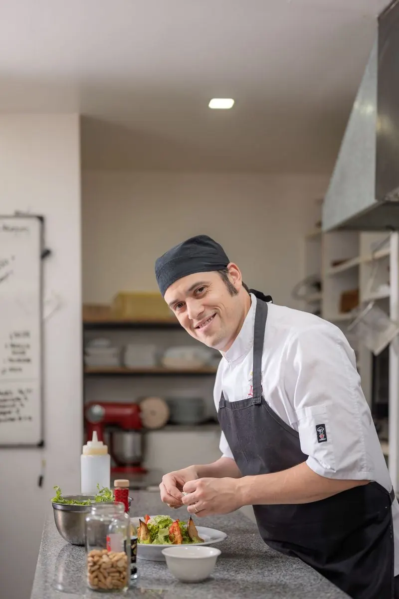 En la cocina de Lares Restó Un cocinero sonríe mientras emplata en la cocina