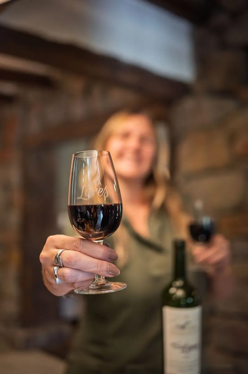 Copa de vino tinto Una mujer del equipo ofrece una copa de vino tinto, con una botella detrás