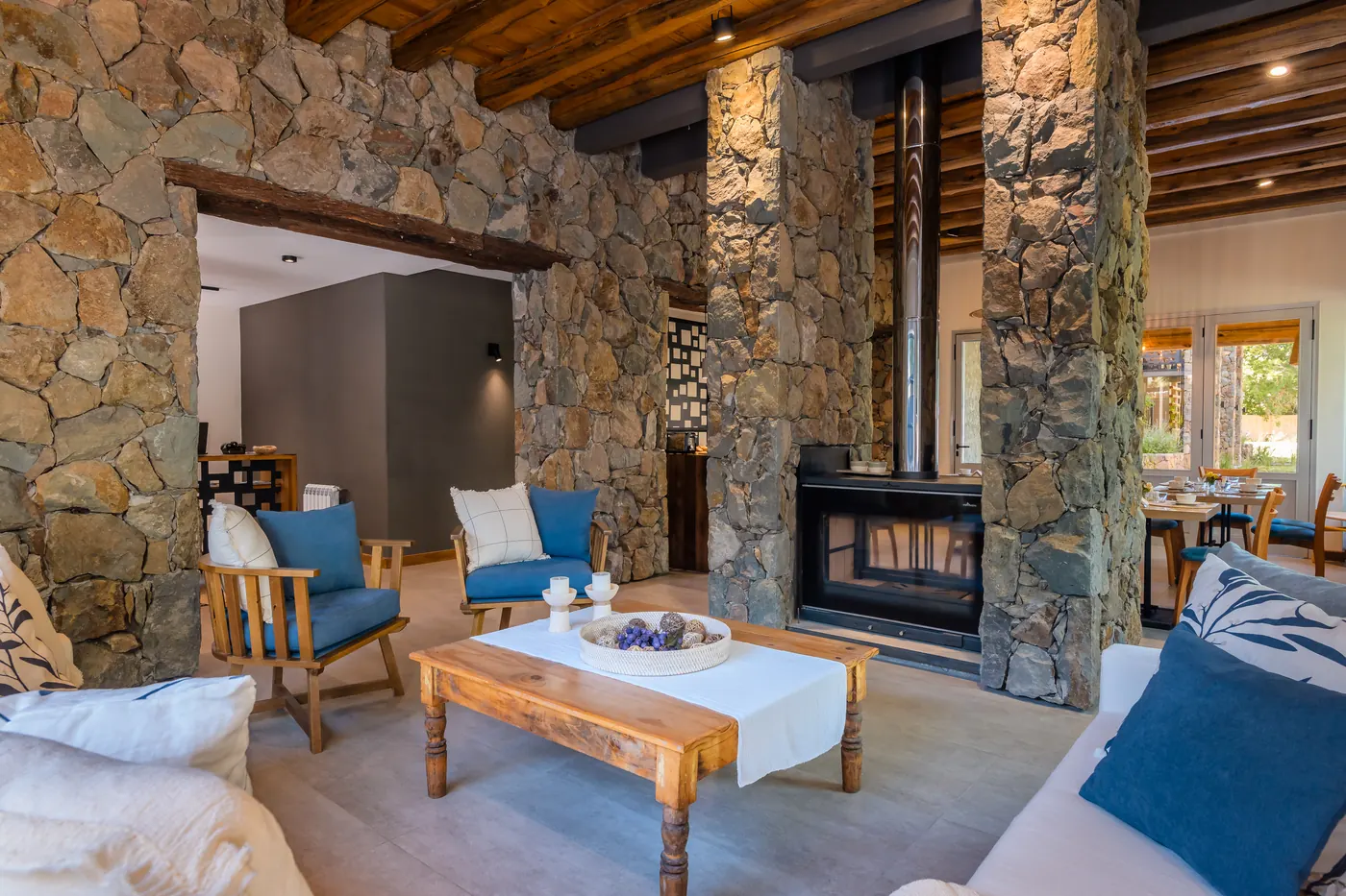 Living de Casa Vita con paredes de piedra, sillones y hogar a leña