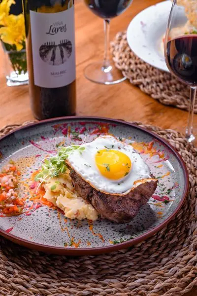 Plato con carne y huevo frito junto a una botella de Viña Lares y copas de vino tinto